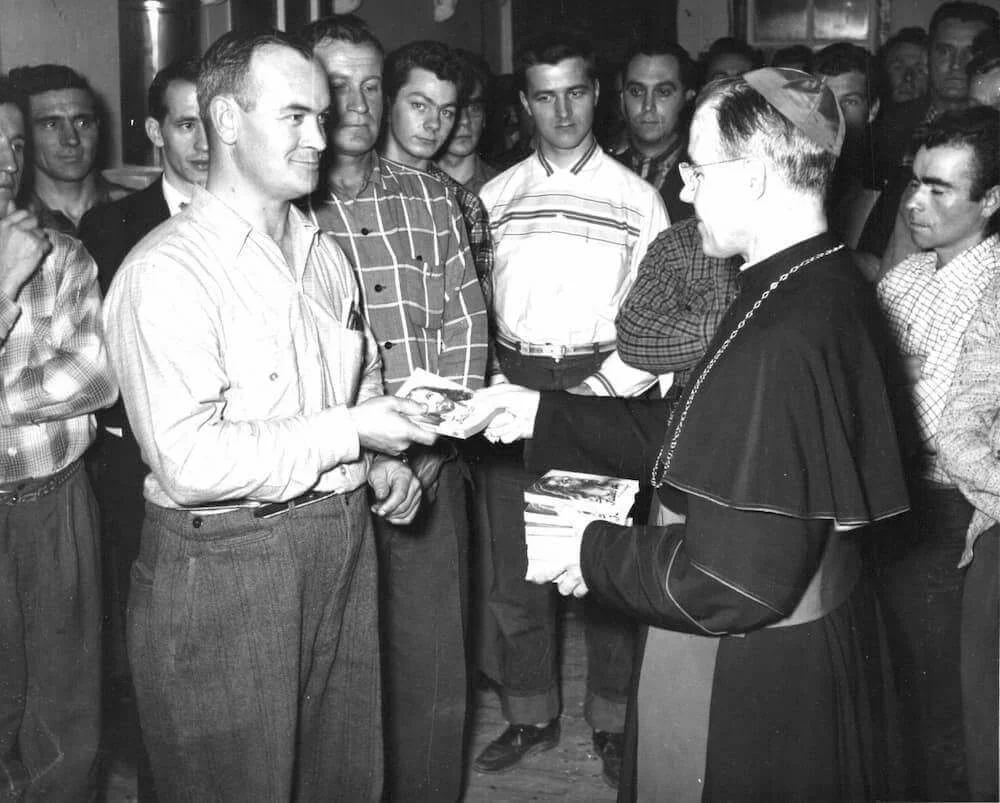 Mgr Couturier remet un document à un travailleur, entouré de bûcherons